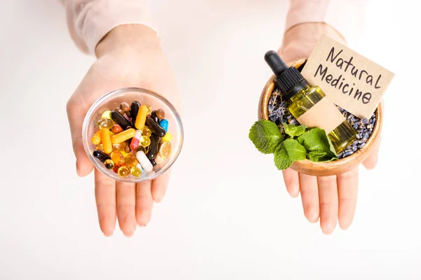 Imagen recortada de la mujer sosteniendo cuencos con aceite de medicina natural y píldoras farmacológicas aisladas en blanco - foto de stock