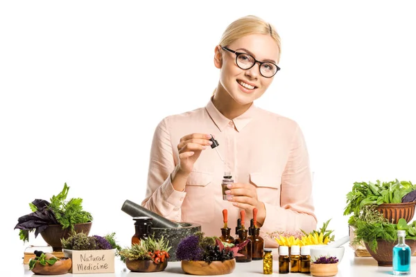 Mujer sonriente en gafas haciendo aceite esencial aislado en blanco y mirando a la cámara - foto de stock