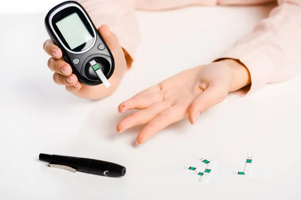 Обрезанное изображение женщины, измеряющей уровень глюкозы в крови глюкометром, выделенный на белом, сахарный диабет — стоковое фото