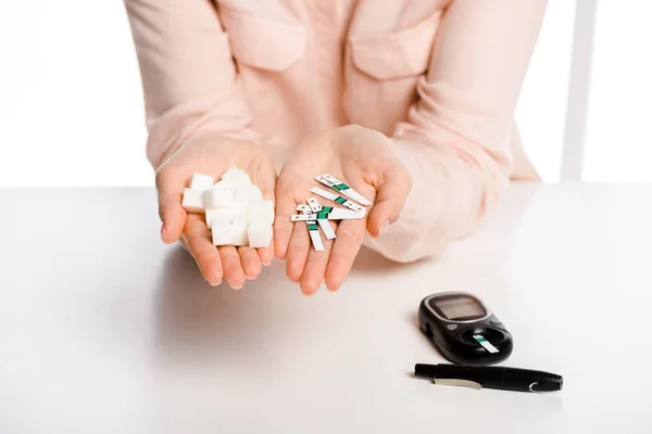 Imagem cortada de mulher segurando tiras de glicosímetro e açúcar refinado em mãos isoladas em branco, conceito de diabetes — Fotografia de Stock