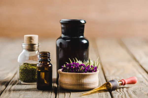 Glass bottles of essential oils and flowers on wooden tabletop, alternative medicine concept — Stock Photo