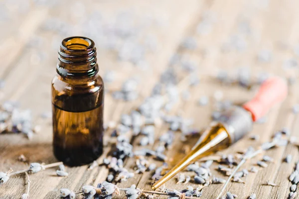 Bottles of essential oil, dropper and scattered herbs on wooden tabletop, alternative medicine concept — Stock Photo