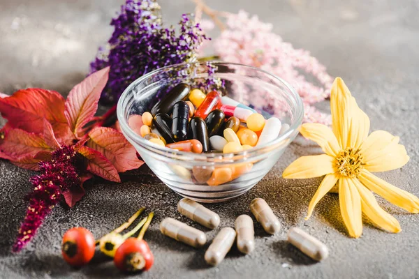 Pastillas farmacológicas en cuenco de vidrio y flores de colores en la mesa de madera, concepto de medicina alternativa - foto de stock