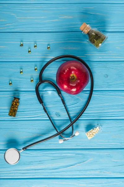 Vue de dessus de pomme rouge, stéthoscope et médicaments de médecine douce sur plateau en bois turquoise — Photo de stock