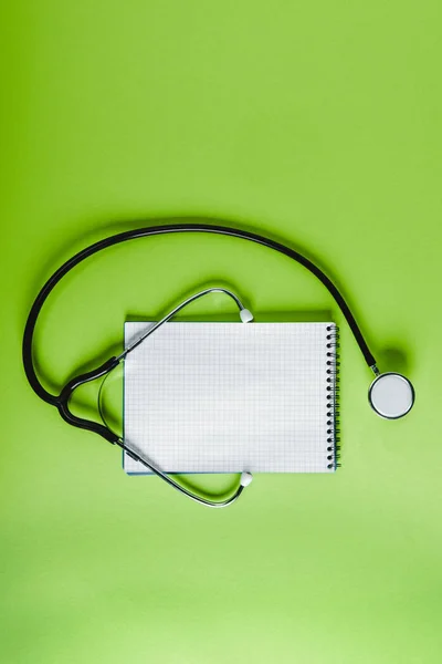 Top view of stethoscope and empty notebook on green surface — Stock Photo