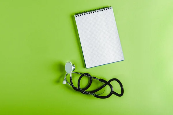 Elevated view of stethoscope and empty notebook on green surface — Stock Photo