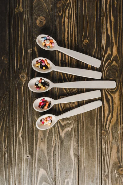 Vista superior de cinco colheres com pílulas na mesa de madeira — Fotografia de Stock