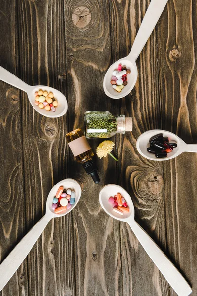 Vue du dessus des cuillères avec des pilules et des bouteilles en verre avec des médicaments alternatifs sur table en bois — Photo de stock