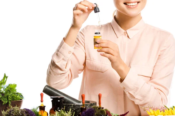 Imagen recortada de mujer sonriente sosteniendo cuentagotas y botella de vidrio con aceite esencial aislado en blanco - foto de stock