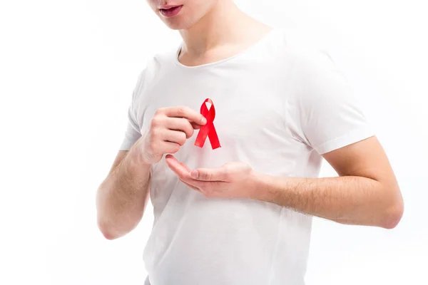 Imagen recortada de un hombre joven que pone cinta roja en la camisa aislada en blanco, concepto del día del sida mundial - foto de stock