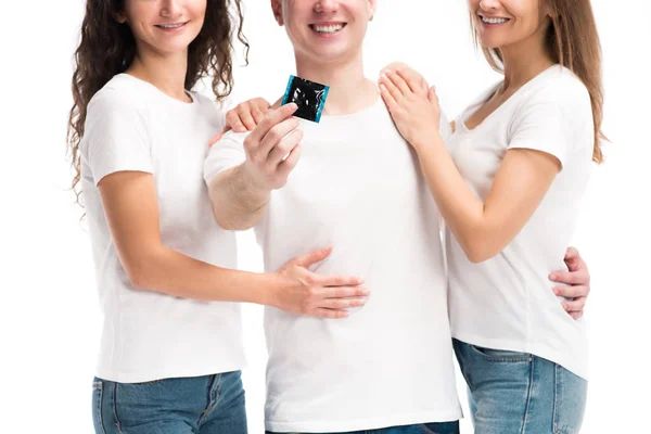 Image recadrée d'un homme souriant montrant un préservatif, deux filles l'embrassant isolé sur blanc, concept de journée mondiale des aides — Photo de stock