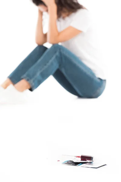 Selective focus of sad woman sitting and touching head isolated on white, condoms and syringe with blood on foreground, world aids day concept — Stock Photo