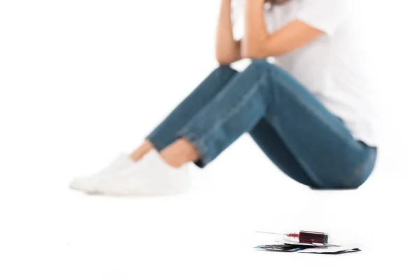 Selective focus of woman sitting isolated on white, condoms and syringe with blood on foreground, world aids day concept — Stock Photo