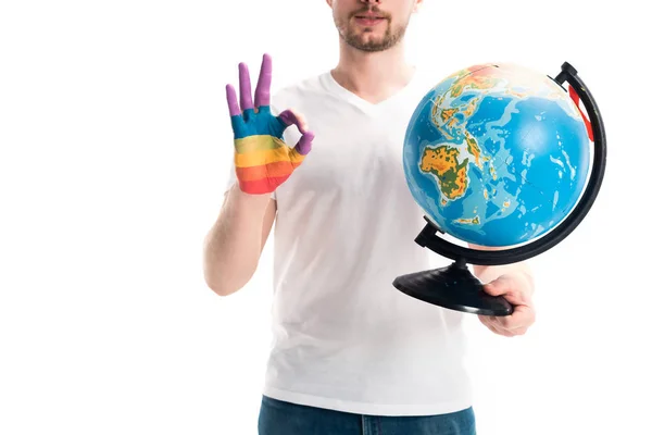 Image recadrée de l'homme tenant globe et montrant un geste correct avec peint à la main en arc-en-ciel isolé sur blanc, concept de journée mondiale des aides — Photo de stock