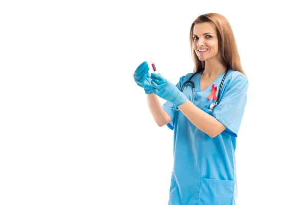 Sonriente atractivo doctor con cinta roja sosteniendo jeringa con sangre aislada en blanco, mundo SIDA día concepto — Stock Photo