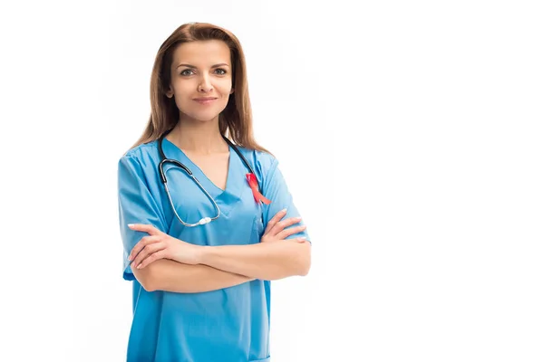 Médecin attrayant avec ruban rouge debout avec bras croisés et regardant la caméra isolée sur blanc, concept de journée mondiale des aides — Photo de stock