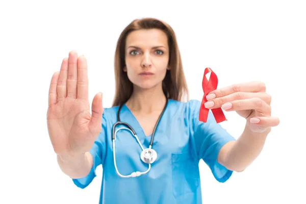 Atractivo médico sosteniendo cinta roja y mostrando gesto de stop aislado en blanco, el mundo SIDA concepto del día — Stock Photo