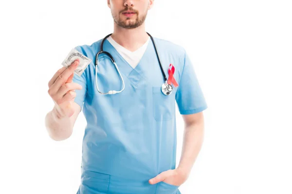 Cropped image of doctor with red ribbon on uniform showing condom isolated on white, world aids day concept — Stock Photo