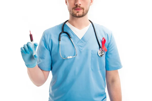 Cropped image of doctor with red ribbon on uniform holding syringe with blood isolated on white, world aids day concept — Stock Photo