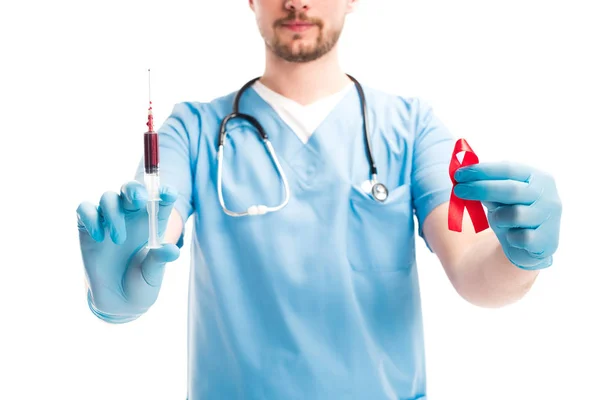 Imagen recortada del médico mostrando cinta roja y jeringa con sangre aislada en blanco, concepto del día del sida mundial - foto de stock