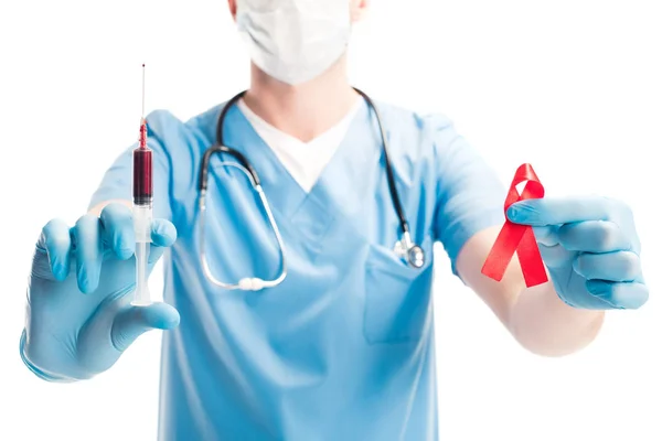 Cropped image of doctor in medical mask holding red ribbon and syringe with blood isolated on white, world aids day concept — Stock Photo