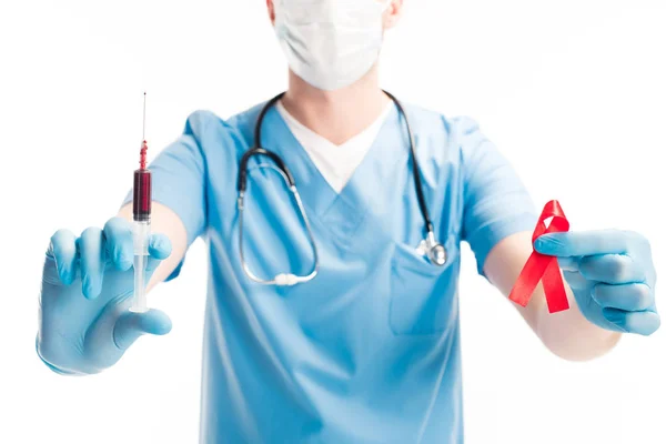 Imagem cortada do doutor na máscara médica que mostra a fita vermelha e a seringa com sangue isolado no conceito branco, do dia das ajudas do mundo — Fotografia de Stock