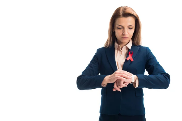 Attractive businesswoman with red ribbon on suit checking time isolated on white, world aids day concept — Stock Photo