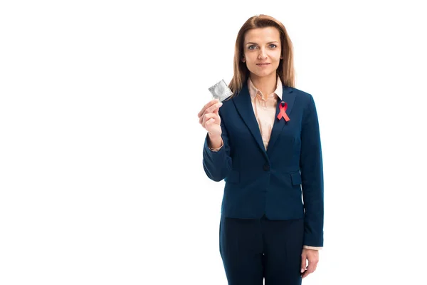 Attractive businesswoman with red ribbon on suit showing condom isolated on white, world aids day concept — Stock Photo
