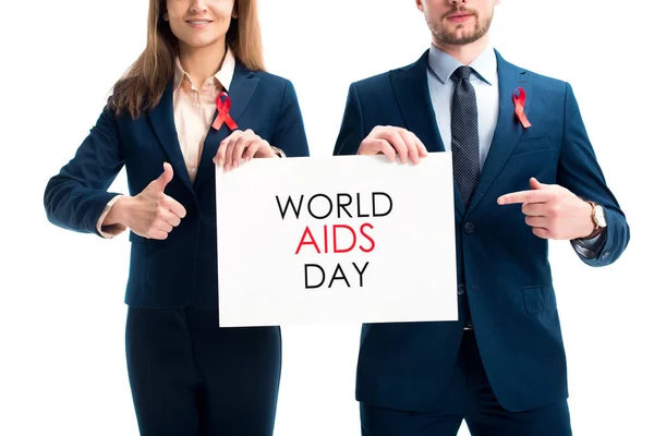 Cropped image of businesspeople with red ribbons on suits pointing on card with world aids day text isolated on white — Stock Photo