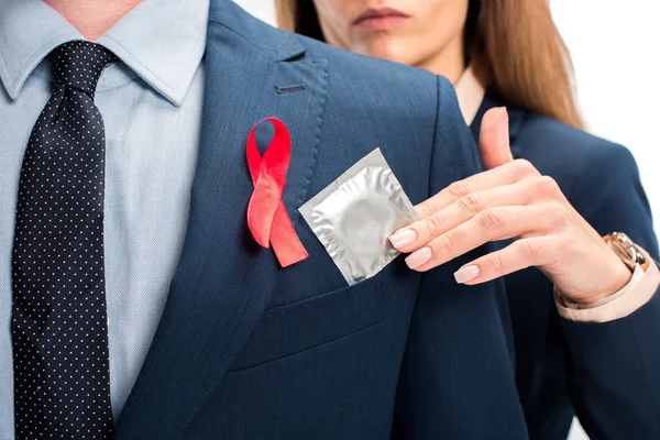 Cropped image of businesswoman giving condom to businessman with red ribbon on suit isolated on white, world aids day concept — Stock Photo