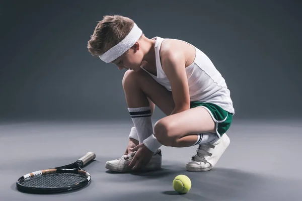 Мальчик-подросток в спортивной форме с теннисной ракеткой и мячом на темном фоне — стоковое фото