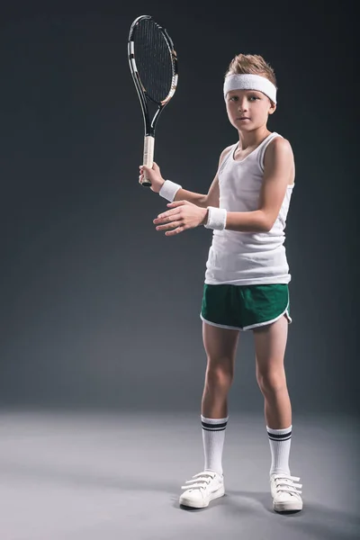 Garçon concentré en vêtements de sport avec raquette de tennis sur fond sombre — Photo de stock