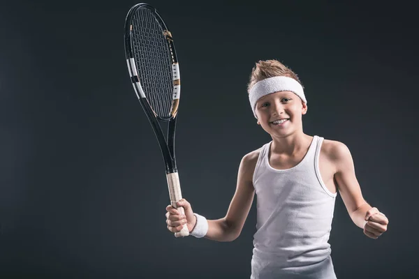 Portrait de garçon souriant en vêtements de sport avec raquette de tennis sur fond sombre — Photo de stock