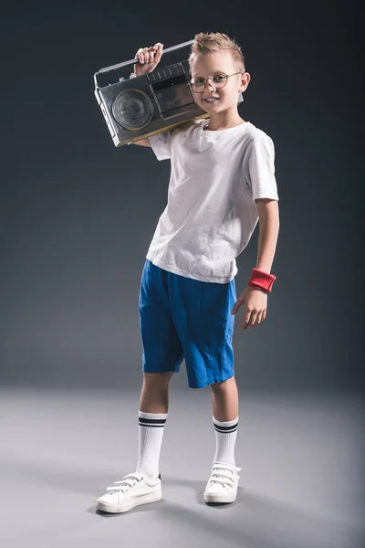Niño preadolescente elegante sosteniendo boombox en el hombro en el fondo gris - foto de stock