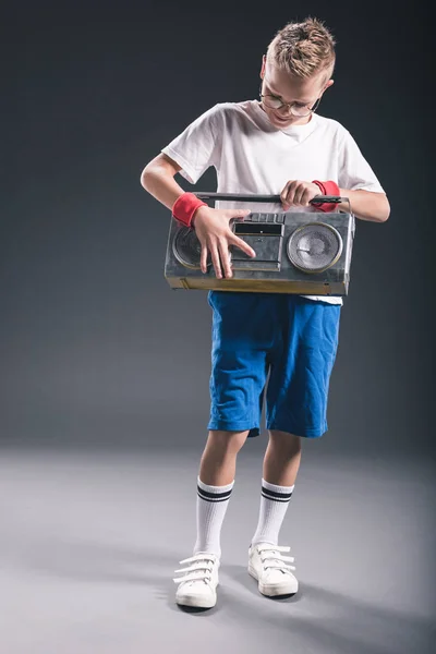 Menino pré-adolescente elegante em óculos segurando boombox no fundo cinza — Fotografia de Stock
