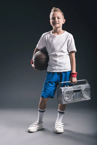 Chico con estilo con pelota de baloncesto y boombox sobre fondo gris - foto de stock