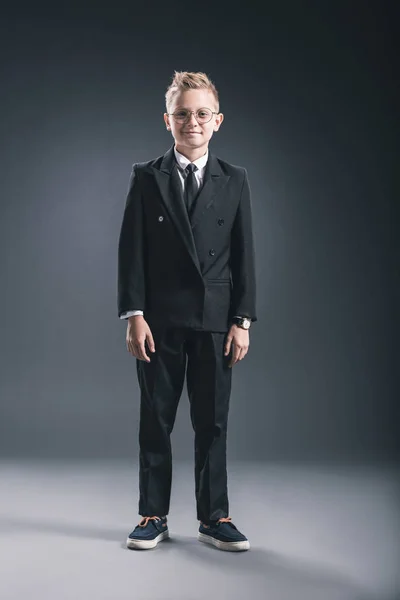 Vorpubertärer Junge, der als Geschäftsmann mit Brille gekleidet in die Kamera auf dunklem Hintergrund blickt — Stockfoto