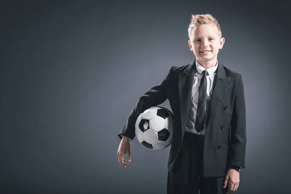 Porträt eines als Geschäftsmann verkleideten Jungen mit Fußballball auf grauem Hintergrund — Stockfoto