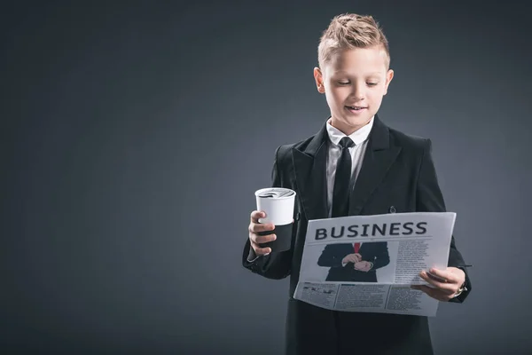 Portrait de garçon en costume d'homme d'affaires avec café pour aller lire le journal d'affaires sur fond gris — Photo de stock