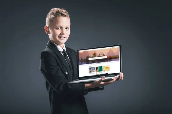 Smiling boy in businessman suit showing laptop with shutterstock website on screen on grey background — Stock Photo