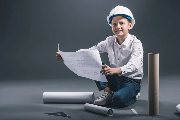 Sorridente ragazzo in casco architetto che tiene cianografie su sfondo scuro — Stock Photo