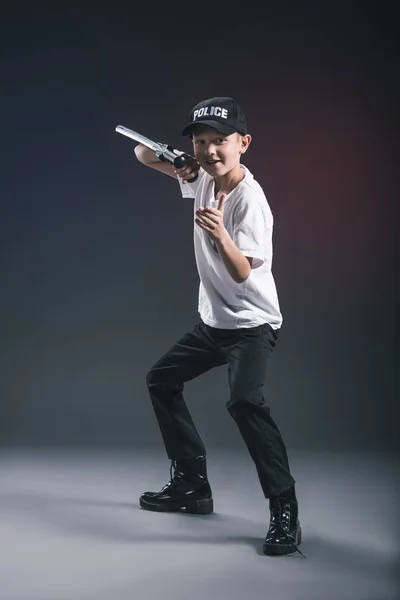 Preteen boy in white tshirt and cap police officer uniform with truncheon posing in dark backdrop — Stock Photo