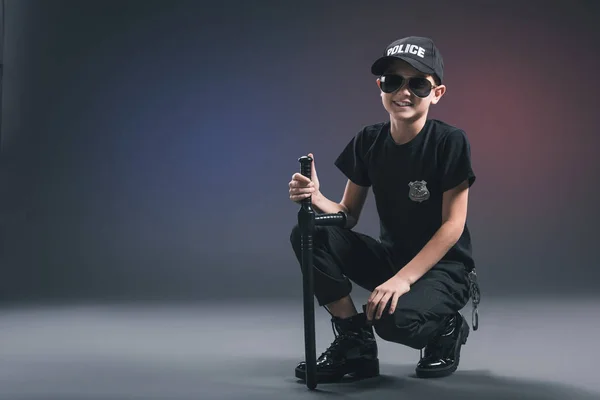 Niño sonriente en uniforme de policía y gafas de sol sobre fondo oscuro - foto de stock