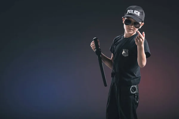 Portrait of boy in policeman uniform and sunglasses gesturing on dark background — Stock Photo