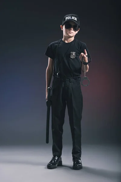 Мальчик в полицейской форме и солнечных очках с наручниками на темном фоне — стоковое фото