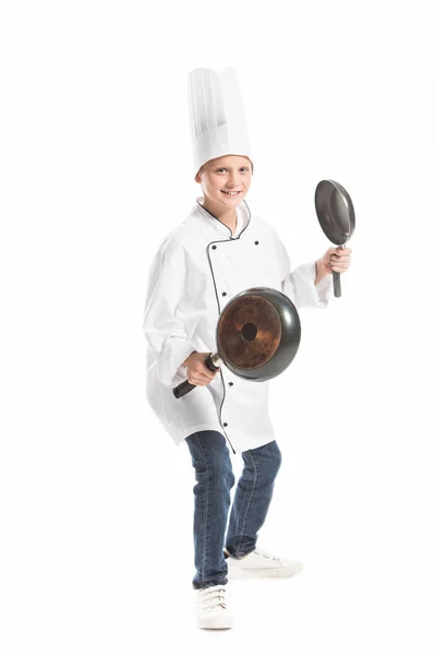 Boy in white chef uniform and hat holding frying pans isolated on white — Stock Photo