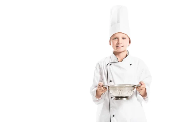 Portrait of smiling boy in white chef uniform with colander isolated on white — Stock Photo