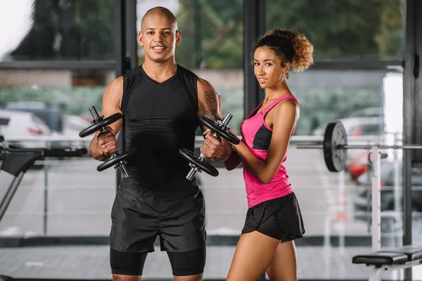 Musclé afro-américain athlète entraînement avec haltères tandis que sa petite amie debout près — Photo de stock