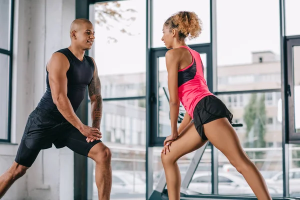 African american couple of athletes looking at each other and doing exercise at gym — Stock Photo