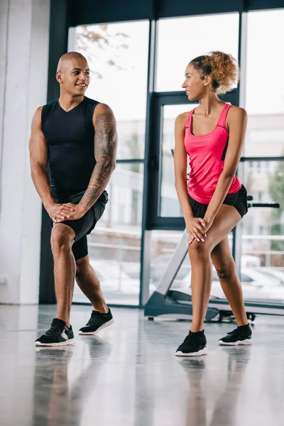 Sorrindo jovem casal de atletas afro-americanos olhando uns para os outros e exercitando-se no ginásio — Fotografia de Stock